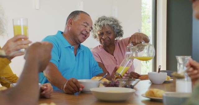 Elderly couple enjoying breakfast together at a wooden dining table, pouring orange juice and sharing a pleasant moment. Ideal for promoting senior living, family health, happiness, and togetherness.