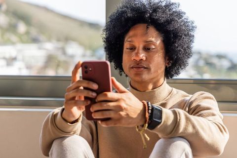 Sunlit african american man using smartphone by window wearing crewneck and watch