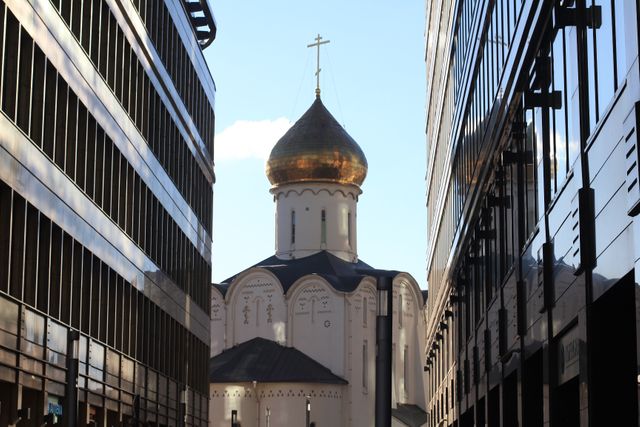 Golden-domed Orthodox cathedral situated between tall modern buildings in urban setting, symbolizing contrast between traditional and contemporary architecture. Ideal for illustrating urban development, juxtaposition of old and new structures, city culture, or spiritual oasis in modern world.