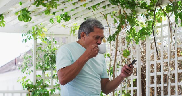 Senior man drinking coffee and using smartphone in garden pergola - Download Free Stock Images Pikwizard.com