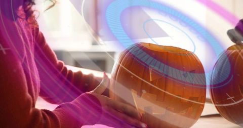 Woman carving jack-o'-lantern with blue digital overlays wearing rust sweater autumn craft