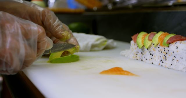 Enhanced view of a chef in kitchen slicing avocado with precision to prepare colorful sushi roll. Perfect for blogs, restaurant promotions, culinary tutorials, or anyone highlighting Japanese cuisine or fresh food preparation.