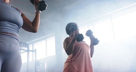 Diverse women lifting hex dumbbells in industrial gym, strength training partners