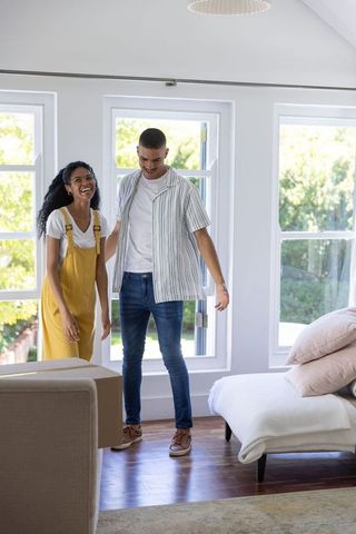 Couple laughing unpacking in bright cozy living room during new home move with natural light