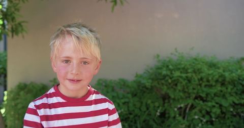 Blond boy wearing red and white striped shirt standing in backyard portrait with copy space
