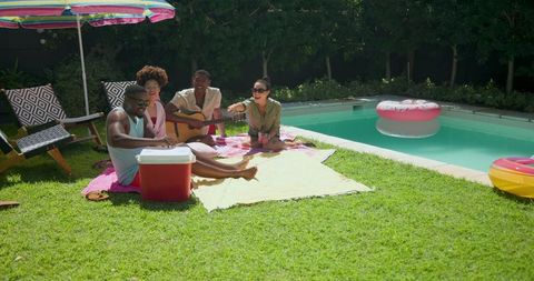 Friends enjoying summer by backyard pool with guitar and cooler