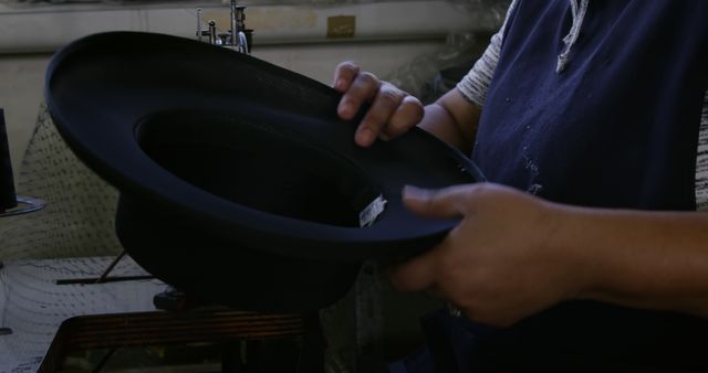 Craftsman carefully making black hat in workshop, highlighting the art of traditional hat-making. Useful for topics on craftsmanship, fashion, artisan work, handmade products, and traditional manufacturing processes.