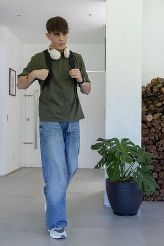 Teenager with backpack and headphones walking through minimal bright home entryway