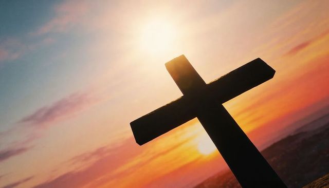 Wooden cross silhouetting against golden sunset over hilltop horizon