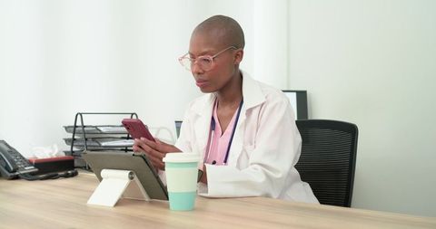 Female clinician checking smartphone and using tablet for patient records in modern clinic