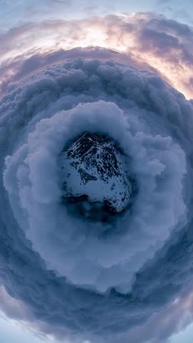Vertical tiny planet aerial video featuring snowy summit encircled by swirling cloud rings at sunris