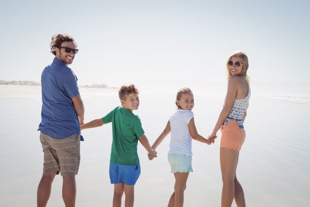 Portrait of family holding hands while standing together on shore at beach during sunny day