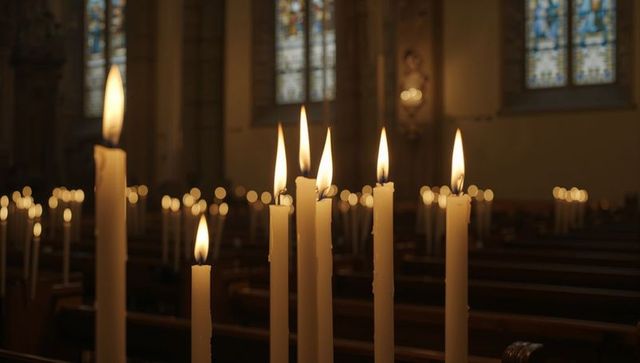 Burning taper candles in church sanctuary casting warm glow with stained-glass background