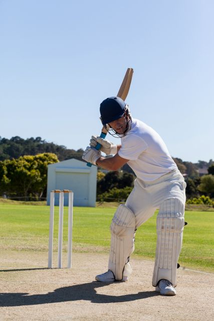 Cricketer in action, batting on a sunny day on a well-maintained field. Ideal for use in sports promotions, cricket training materials, athletic gear advertisements, and articles about cricket or outdoor sports.