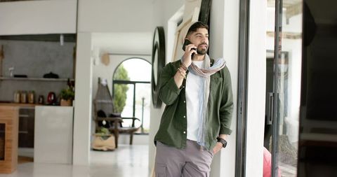 Indian man talking on phone by sliding glass door in bright minimalist open-plan home