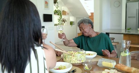 Multigenerational african american women toasting over pasta salad in sunny kitchen