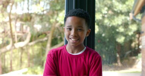 African american boy smiling with folded arms by glass door wearing red long-sleeve shirt