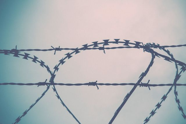 Barbed wire stretching across a cloudy sky, symbolizing confinement and security. Ideal for use in articles about security measures, prison systems, or the concept of boundaries and restrictions.