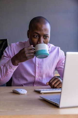 Focused Man at Desk Sipping Coffee While Working on Laptop