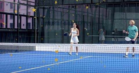 Mixed padel players on blue urban court, woman walking holding paddle by glass wall