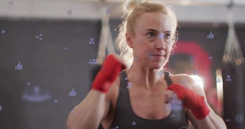 Female boxer training with red hand wraps, social media overlay, focused determination