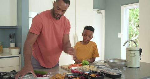 African american father and teenage son preparing healthy meal-prep on kitchen island