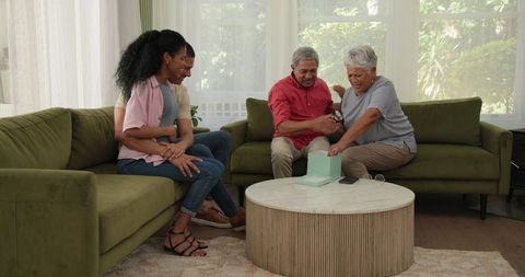 Elderly couple opening gift with family in cozy living room