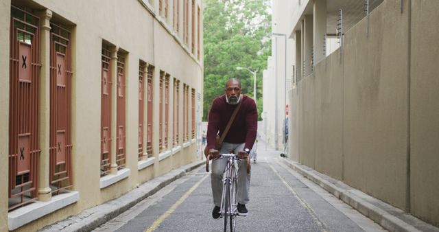 Man riding bicycle through narrow urban alleyway during daytime. Long, narrow passage with tall buildings on each side. Perfect for concept of urban commuting, active lifestyle, city transport, sustainable travel.