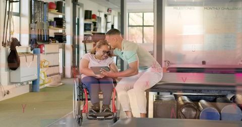 Therapist guiding woman in wheelchair using tablet during rehabilitation clinic session