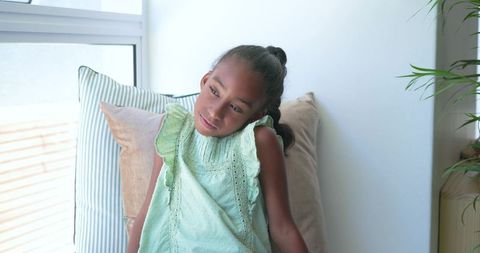 Young girl relaxing and daydreaming in sunlit window seat wearing mint green ruffled dress