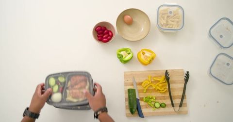 Packing healthy meal prep box with grilled chicken, cucumber, peppers and pasta