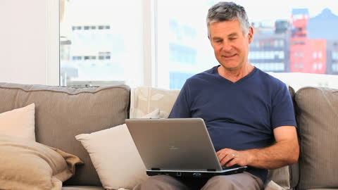 Older Man Relaxing on Sofa Using Laptop