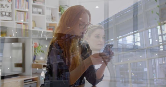 This photo shows two women, one using a smartphone and the other appearing blurred in the background, with overlays of a modern, glass-walled office. It depicts themes of multitasking, technology usage, focus, and collaboration in a contemporary workspace. This image can be effective for illustrating articles about modern work environments, coworking spaces, remote work, and the integration of technology in professional settings.