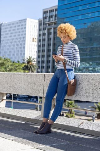 African american woman leaning on urban terrace using smartphone and smartwatch during daylight