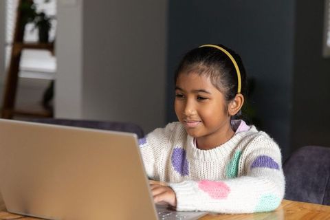 Indian girl studying on laptop at home smiling while using computer for online learning