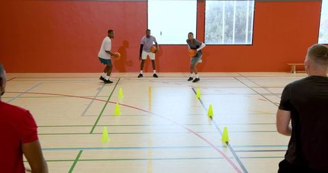 Dribbling basketballs during cone drill by diverse men in indoor gym training session