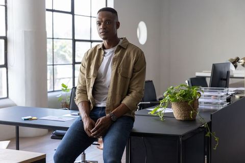 African american professional sitting on desk in modern open-plan office workspace