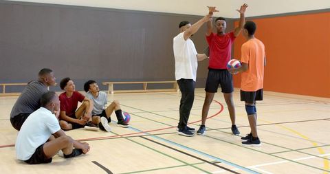 Youth volleyball team watching african american coach demonstrating blocking drill in gym