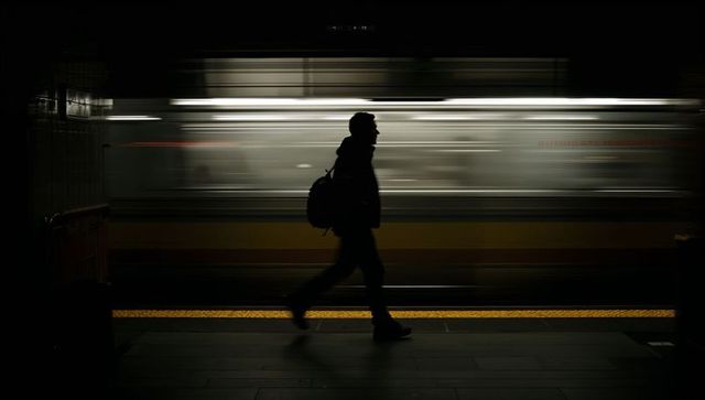 Silhouette commuter walking past blurred train on subway platform at night