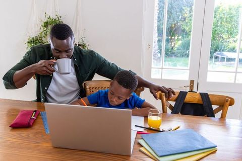 African american father helping son with homework while drinking coffee at dining table