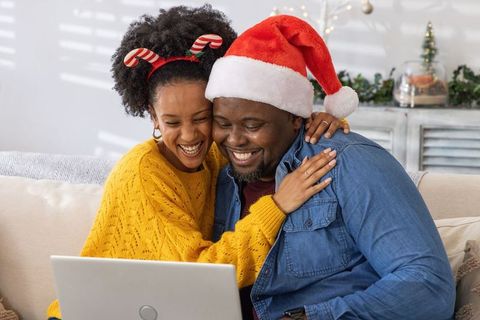 African american couple laughing, sharing laptop, wearing santa hat and festive headband