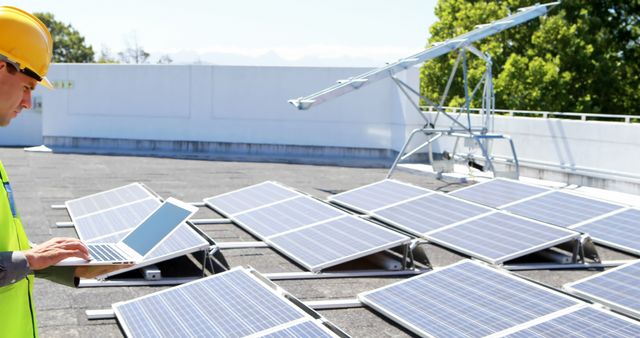 An engineer wearing a hard hat and safety vest is checking solar panels on a rooftop with a laptop. This scene depicts the implementation and maintenance of renewable energy solutions. Ideal for use in articles and promotions about renewable energy, sustainability, green technology, energy efficiency, and modern engineering practices.