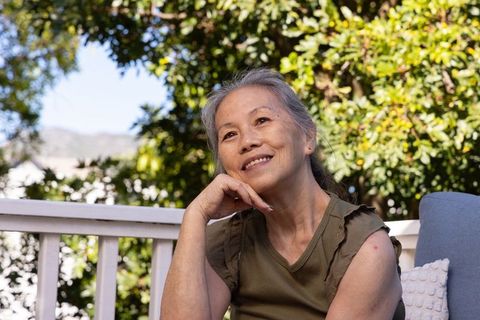 Senior asian woman relaxing on porch, smiling and looking upward, peaceful outdoor portrait
