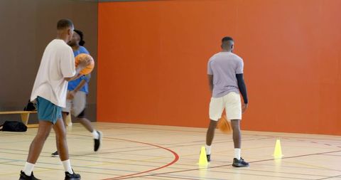 Basketball players practicing agility drills with cones and balls on indoor gym court