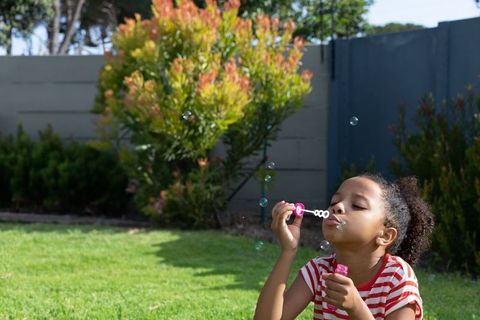 Girl blowing bubbles outdoors in bright daytime scene