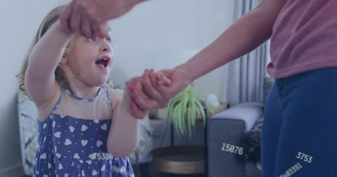 Mother and daughter spinning laughing and holding hands at home in blue heart print dress