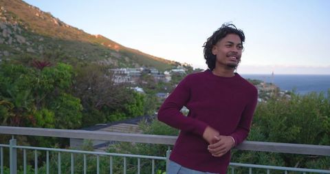 Young man leaning on railing gazing at ocean from coastal terrace during golden hour