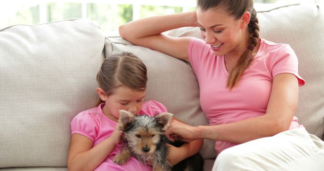 Cute little girl with mother playing with yorkshire terrier puppy at home in the living room