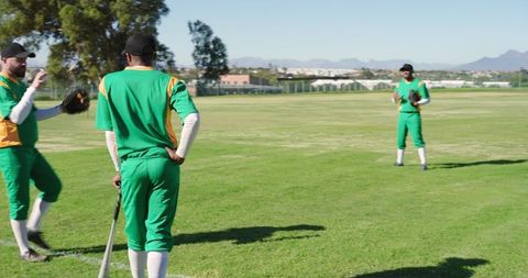Green-uniformed baseball teammates standing in outfield during sunny practice session