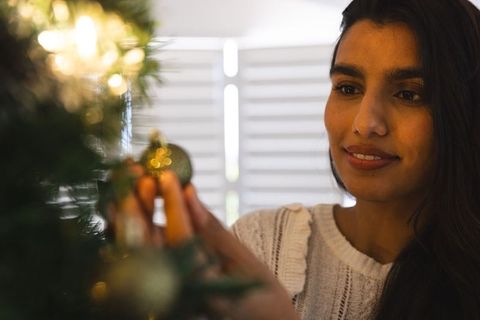 Asian Woman Decorating Christmas Tree Indoors with Golden Ornament